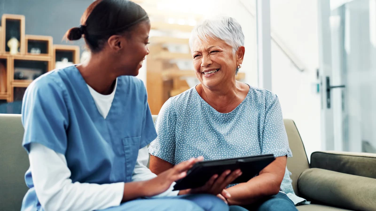 A caregiver and a smiling senior resident reviewing a tablet together in a senior living community