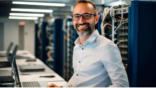 Caucasian IT professional admin using laptop computer doing data transfer operation with rack server cabinets in digital room of data center. Cyber security.