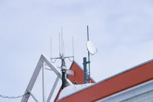 Small satellite dish antenna นn rooftop behind building dark cloudy sky is background. Antenna communication technology. Telecommunication link 5G Digital Transformation connect to data Internet.